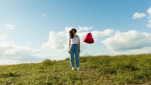 Woman in White Shirt and Denim Pants Holding a Red Balloon