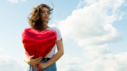 Woman in White Shirt Holding a Red Metallic Balloon