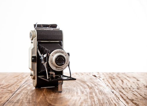 Free Close-up of a vintage folding camera on a wooden table with white background. Stock Photo