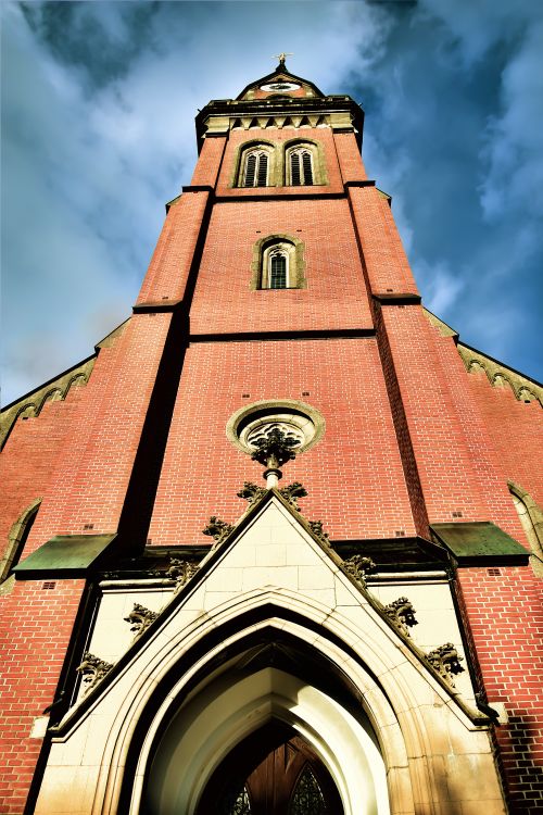Free A low angle view of a historic church tower with red brick exterior against a bright blue sky. Stock Photo