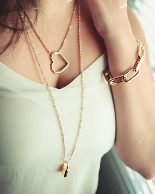 Free Close-up of woman wearing gold heart-shaped necklace and chunky bracelet. Stock Photo