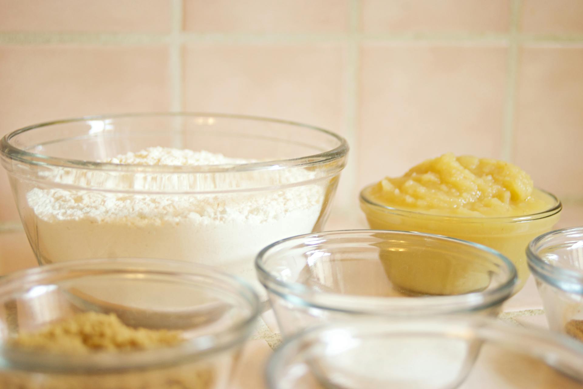 A close-up view of baking ingredients like flour and applesauce in glass bowls on a kitchen countertop.