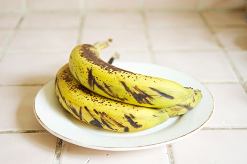 Free Two ripe, spotted bananas on a white ceramic plate on a tiled surface, indoors. Stock Photo