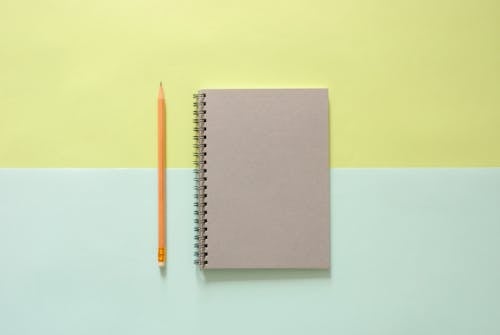 White Spiral Notebook Beside Orange Pencil