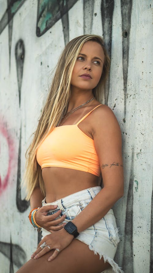 Photo of a Beautiful Woman in an Orange Crop Top Leaning on a Wall
