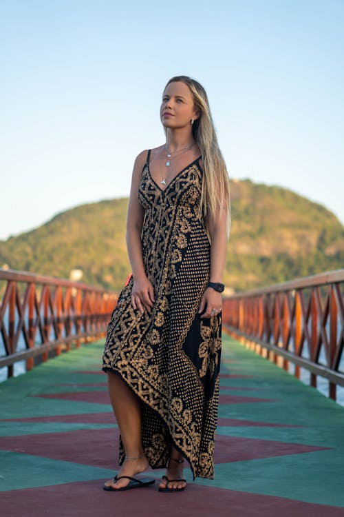 Woman in a Black and Gold Dress Standing on a Bridge