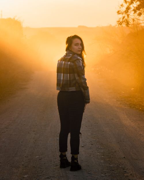 Free A woman stands on a foggy dirt road during sunrise, creating a serene countryside scene. Stock Photo