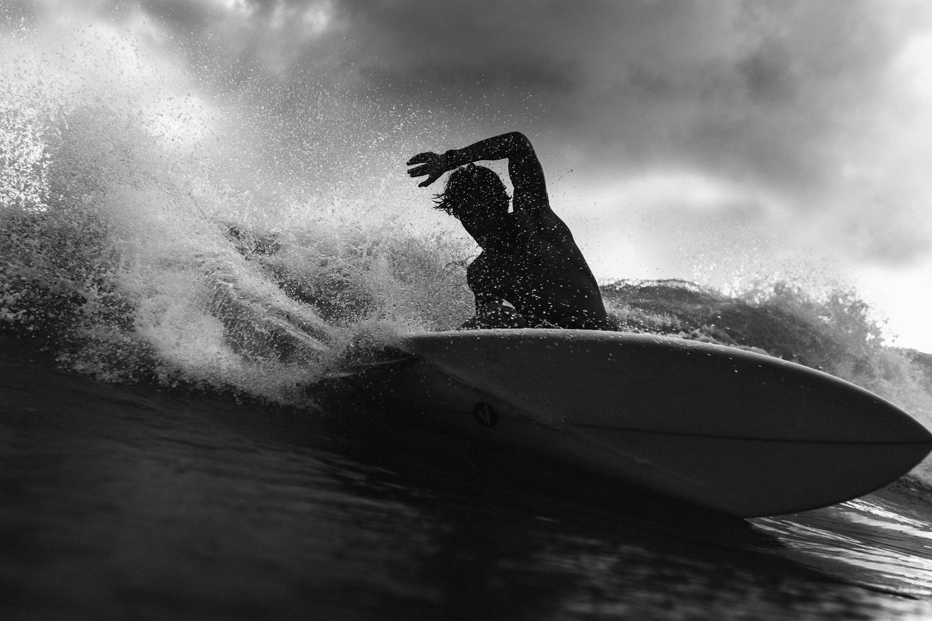 Black and white of anonymous male surfer riding on wave with raised arm against cloudy sky in stormy weather outside