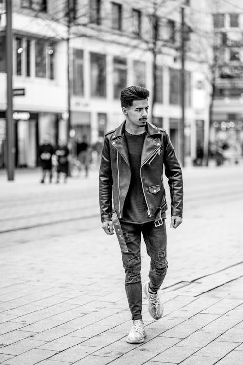Free Grayscale Photo of a Man in a Leather Jacket Walking on the Street Stock Photo