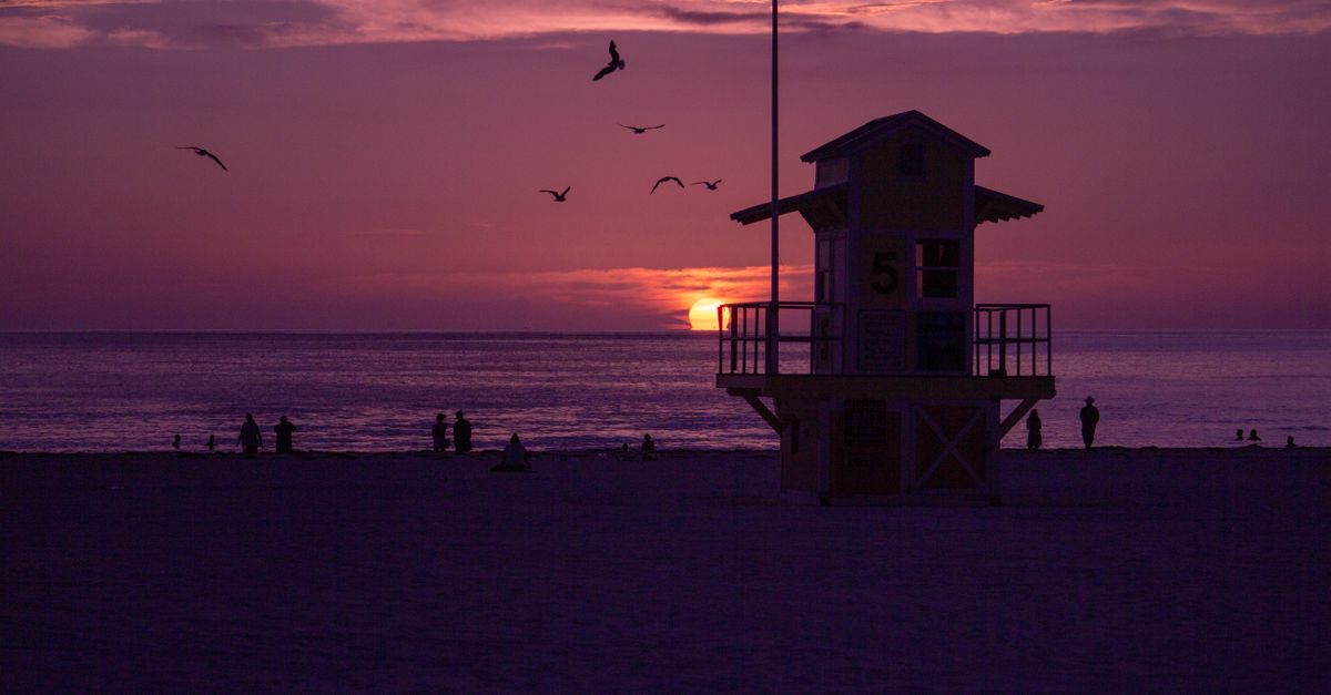 Silhouette of lifeguard tower at Clearwater Beach during a vibrant sunset with birds in the sky.