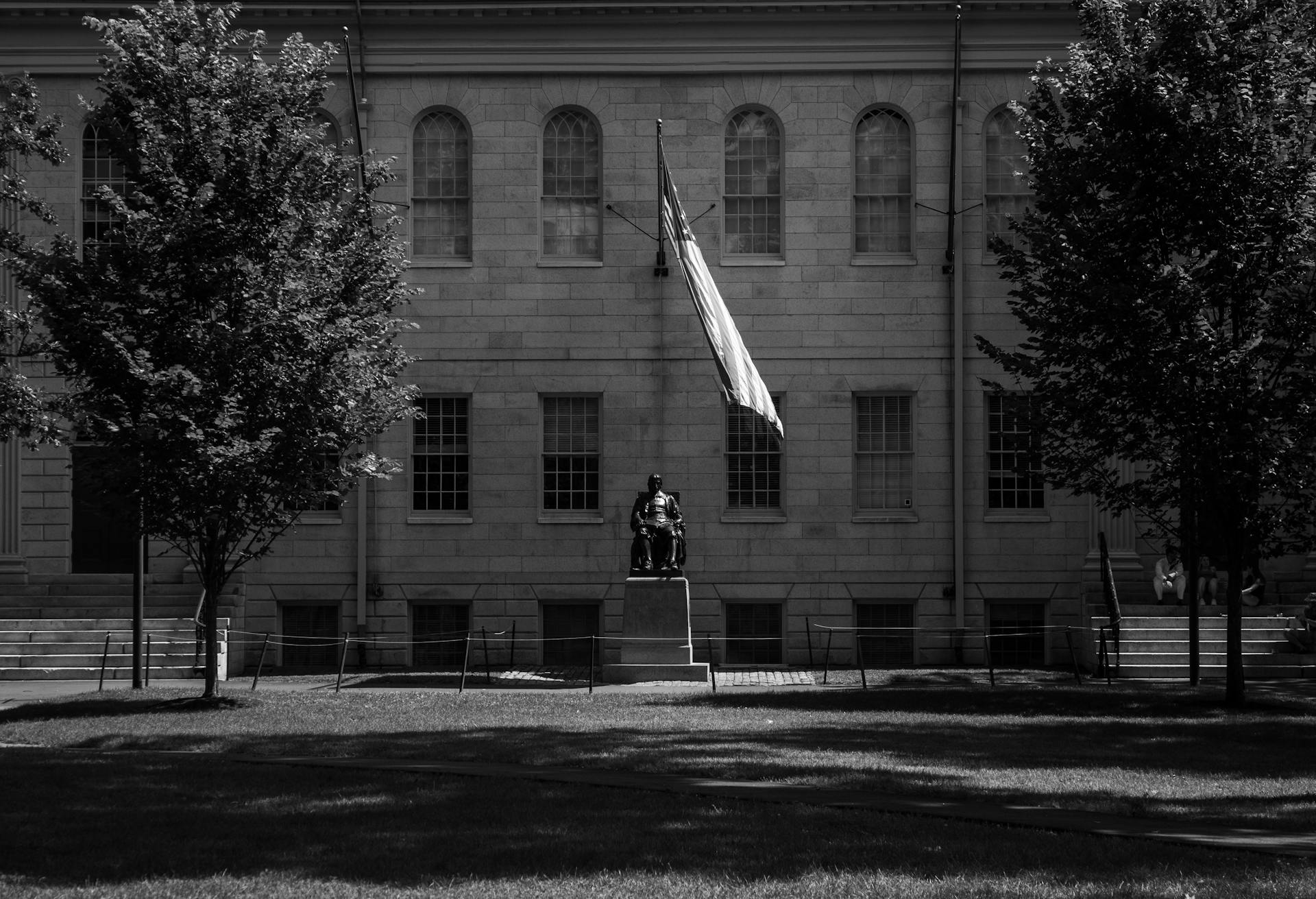 Grayscale photo of John Harvard statue at Harvard University in Cambridge, MA.