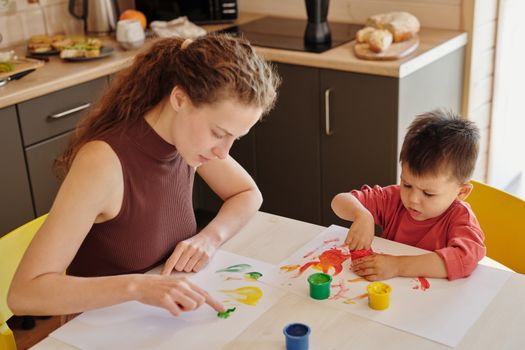 A mother and child engage in creative finger painting at a kitchen table, fostering creativity and family bonding.