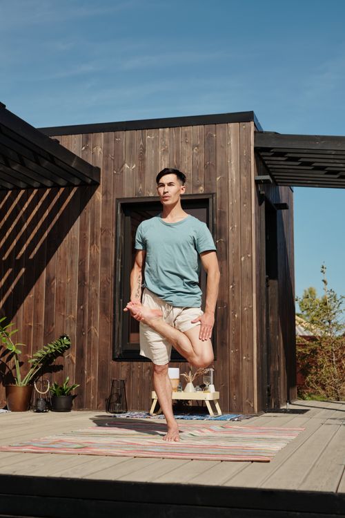 Free A man performs a yoga pose on a wooden veranda, emphasizing a healthy lifestyle. Stock Photo