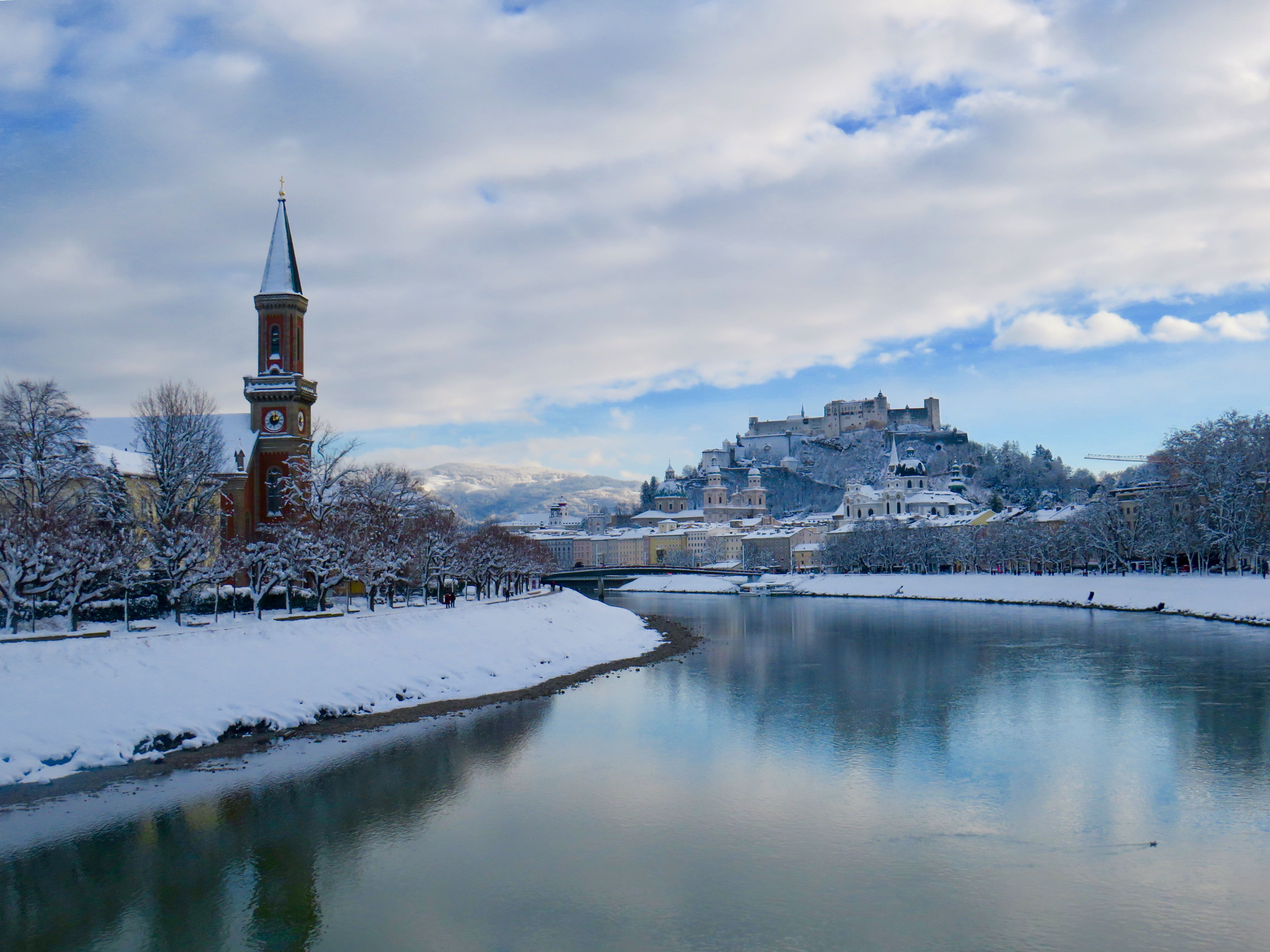 A snow-covered Austrian city with baroque domes and a fortress on the hill above it