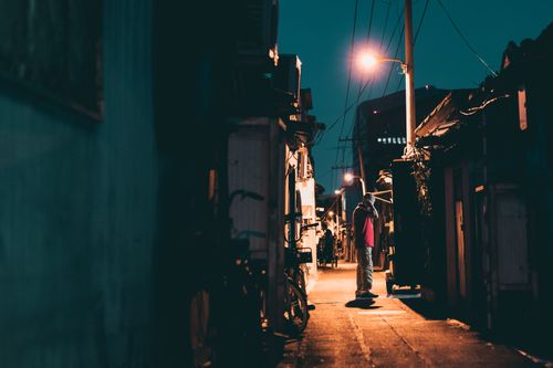Free A person standing in a narrow, dimly lit alleyway in Beijing at night, surrounded by houses and lampposts. Stock Photo