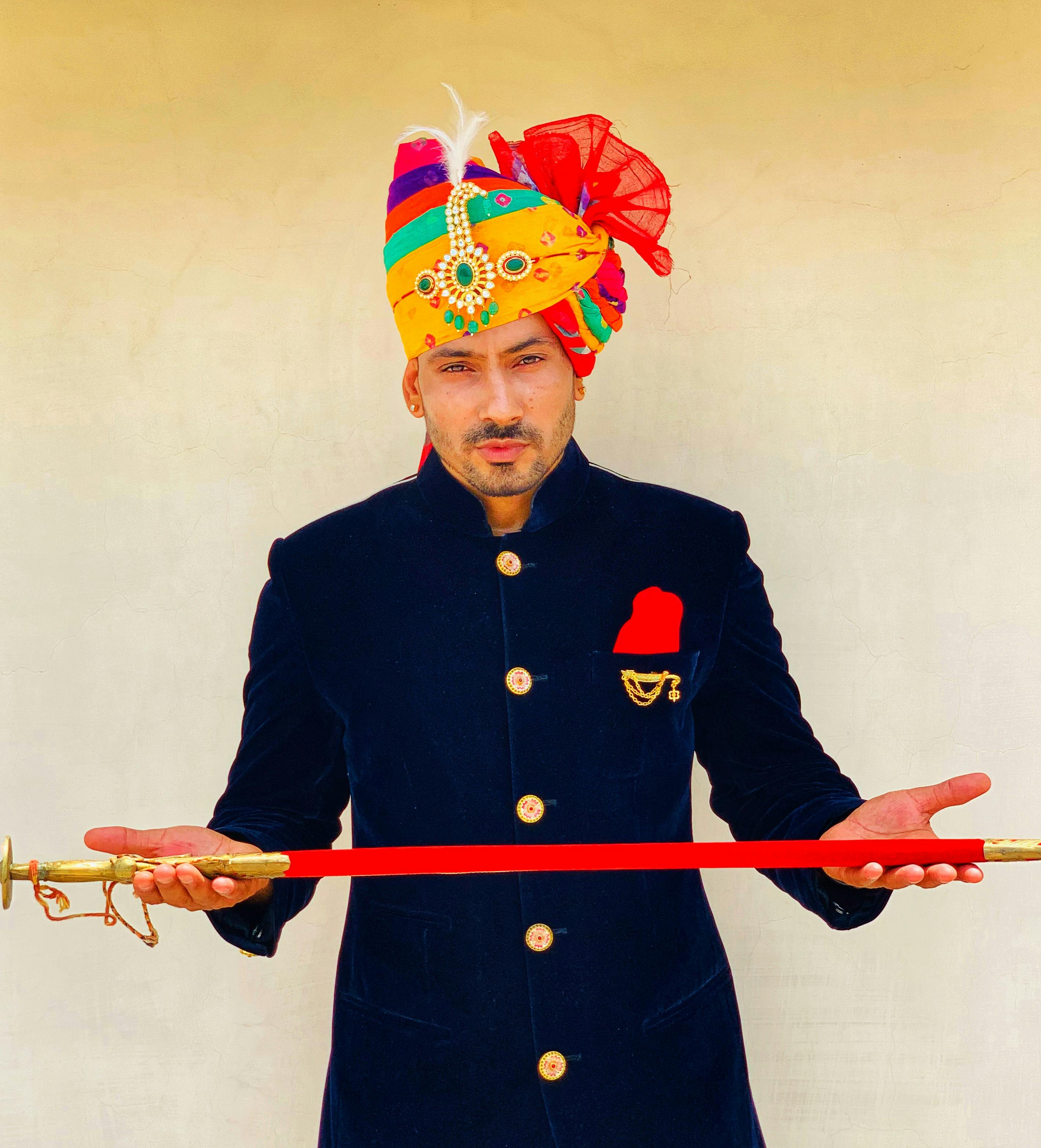A man in a vibrant turban and traditional attire holds a decorative sword in Jaipur, India.
