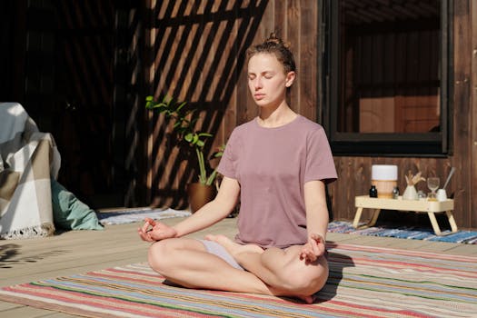 Woman practicing meditation in lotus pose on a sunny outdoor deck.