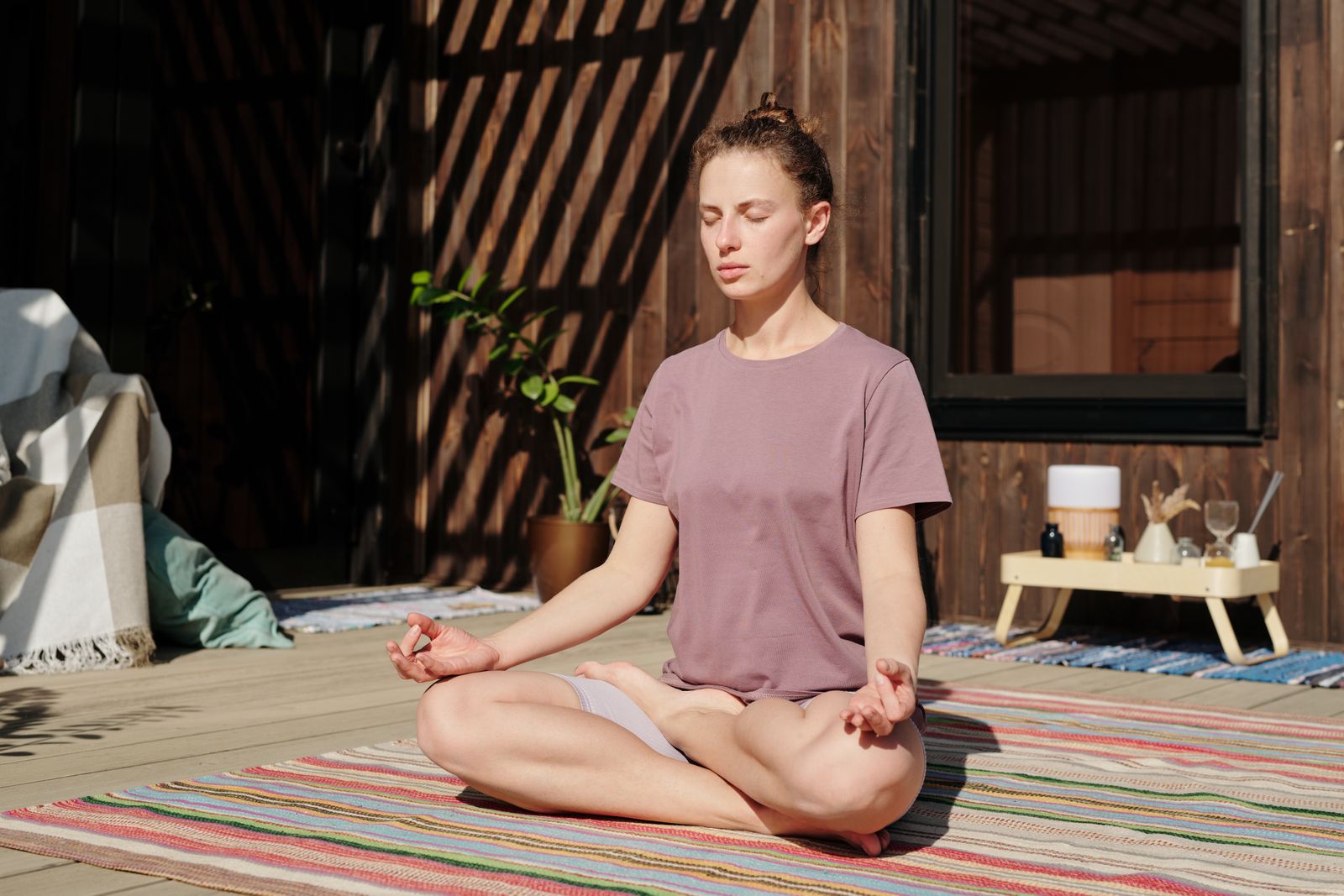 Woman practicing meditation in lotus pose outdoors on a deck, illustrating steady practice for stilling chitta vritti