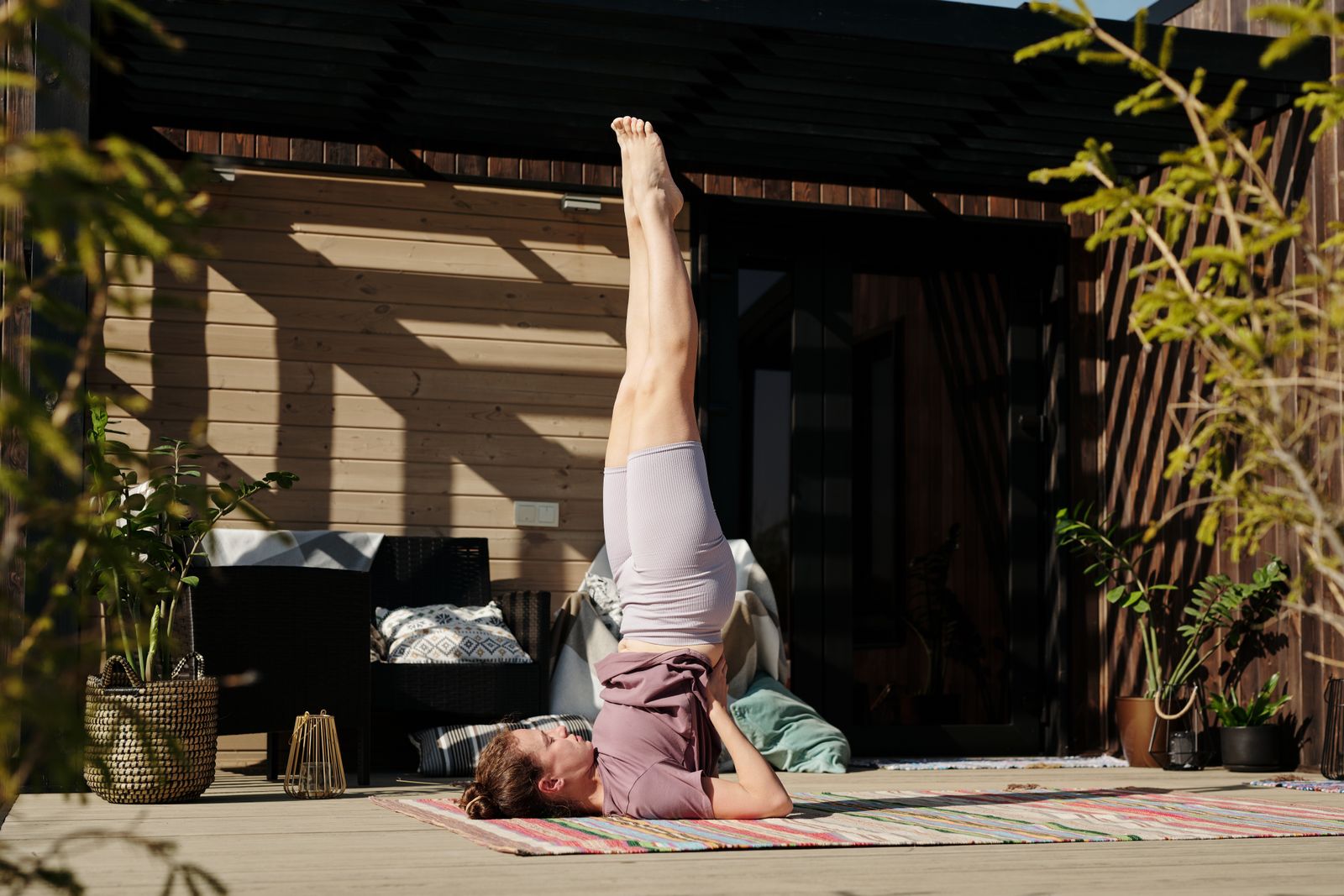Woman performing a supported shoulder stand yoga pose outdoors on a sunny patio