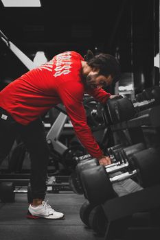 Athletic man in red long sleeves working out indoors in a gym with dumbbells.