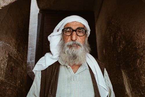 Free From below of senior bearded ethnic male in eyeglasses with wrinkled skin looking at camera in old building Stock Photo