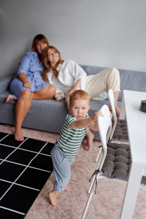 Free From above of cute barefoot baby near chair and relatives resting on couch in living room Stock Photo