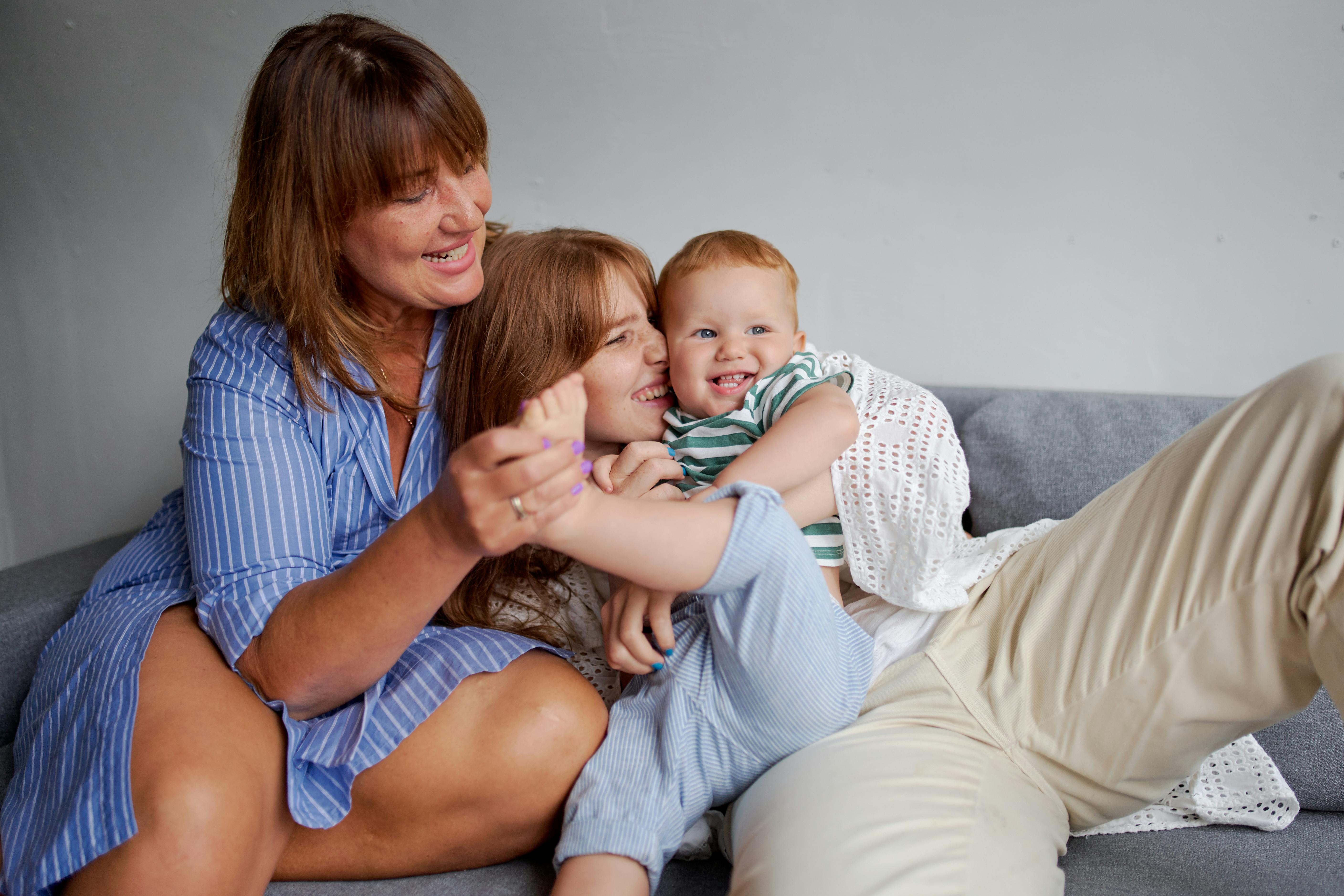 cheerful women playing with toddler child on sofa