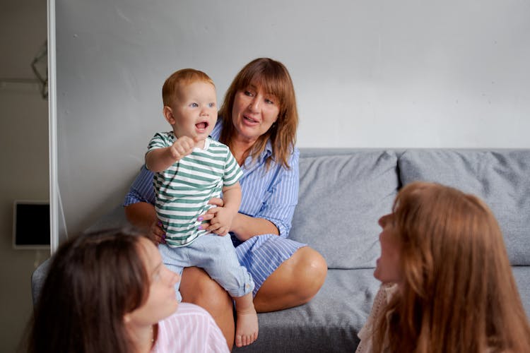 Smiling Grandma With Little Boy On Sofa Near Daughters