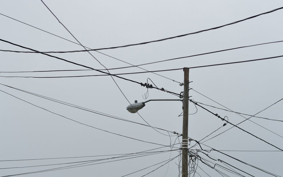 A view of intersecting power lines and a street lamp on a cloudy day, creating a complex visual pattern.