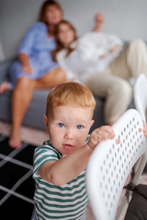 Free From above of adorable little boy in striped wear looking at camera near women on sofa Stock Photo