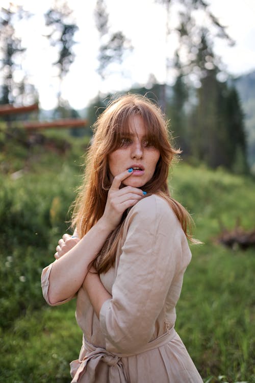 Young pondering female in casual outfit looking away near greenery hill under glowing sky in summer