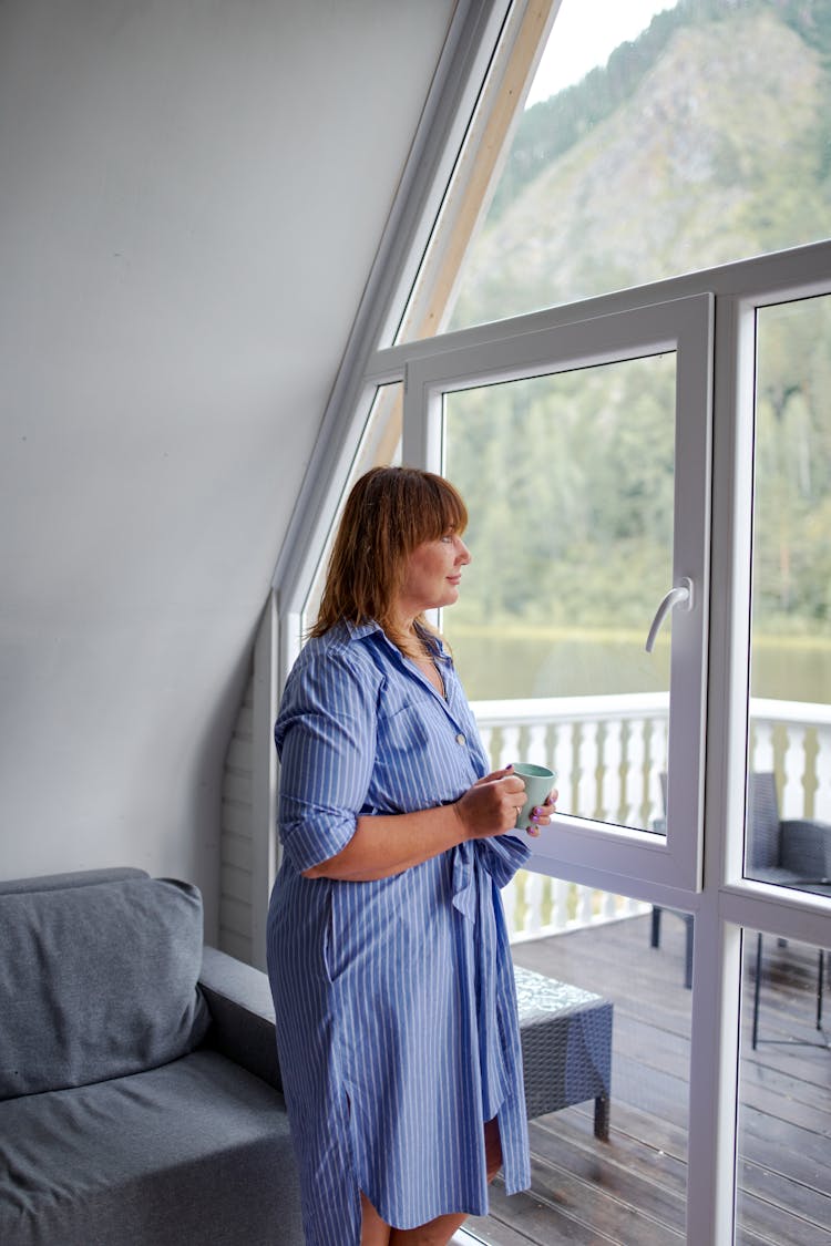 Mature Woman With Cup Near Glass Wall At Home