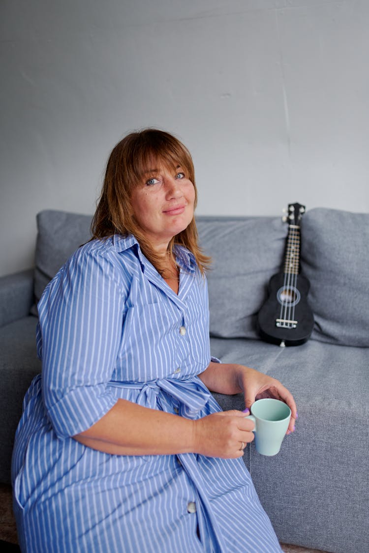 Smiling Mature Woman With Cup Of Beverage On Sofa