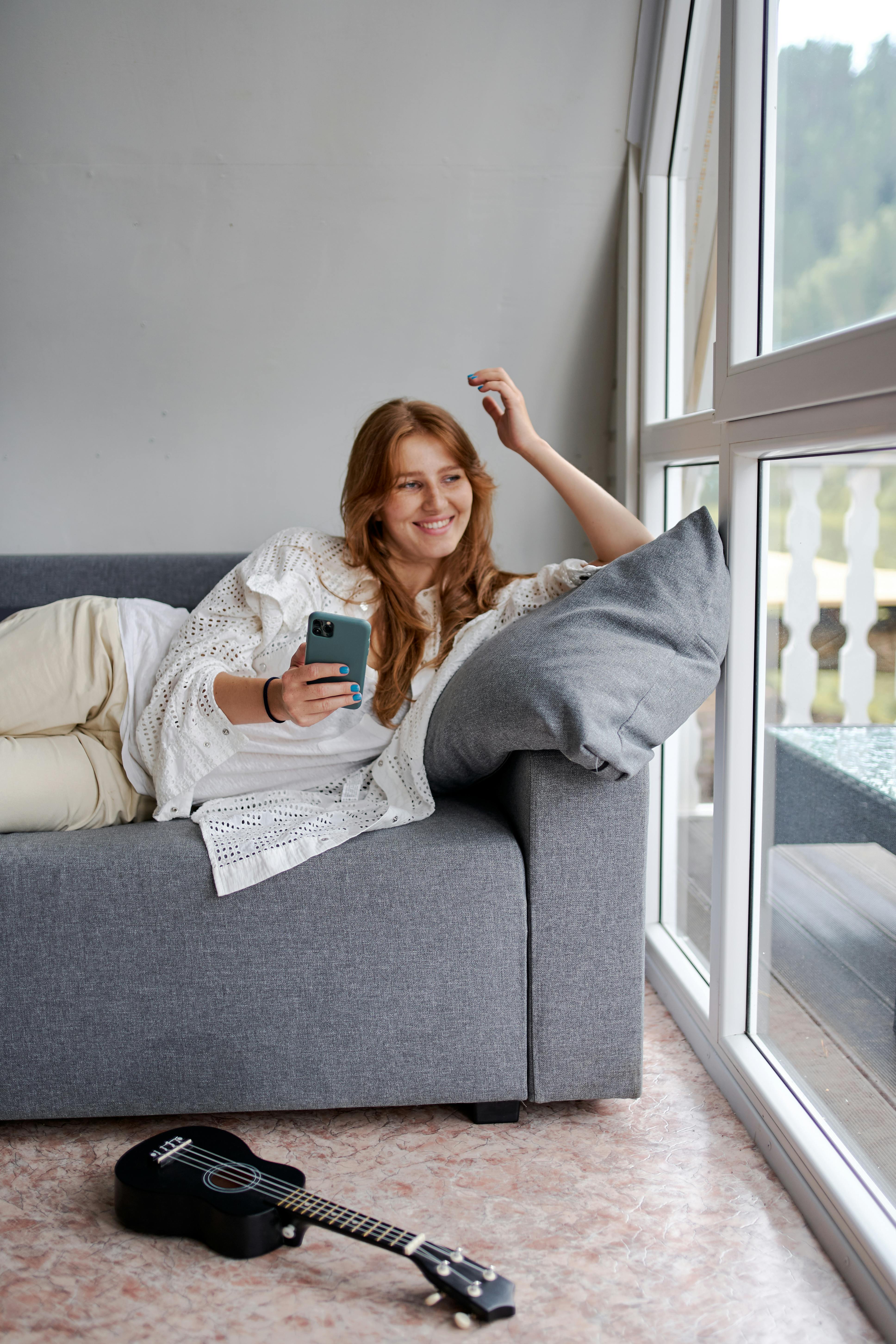 smiling woman with smartphone lounging on sofa in house