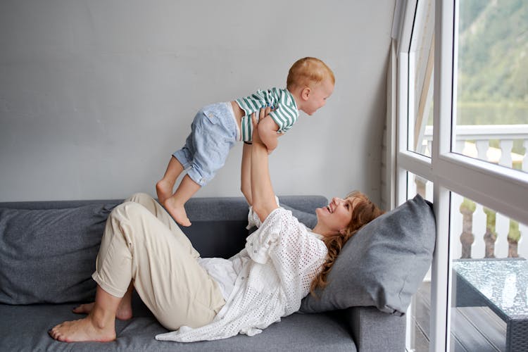 Cheerful Woman Raising Unrecognizable Baby On Couch At Home