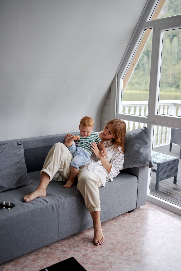 Mother Playing With Smiling Boy On Sofa At Home