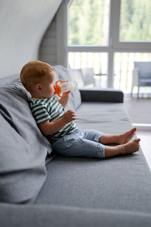 Cute toddler child drinking water on sofa in house