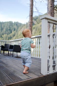 一个赤脚小男孩在绿树山的木阳台上散步的匿名背影