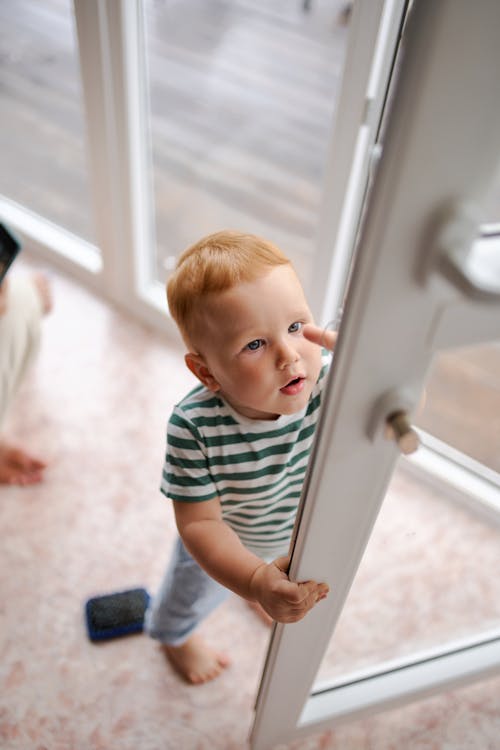 Free From above of little read haired little boy curiously trying to reach door handle Stock Photo