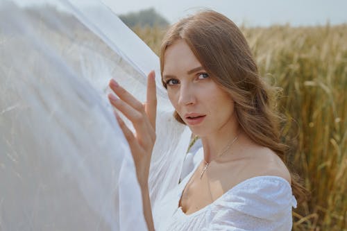 Tender young woman standing on field near waving white veil