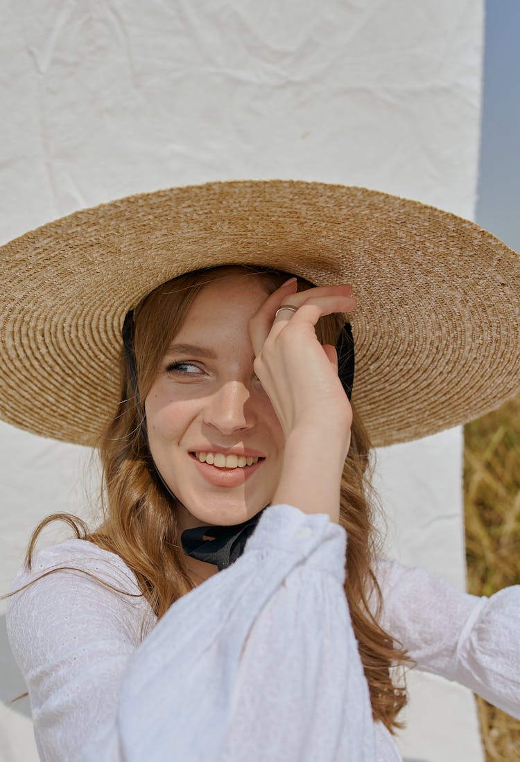 Cheerful Woman In Hat Standing Near White Sheet In Countryside