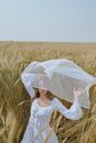 Serene trendy woman standing on field under waving white veil