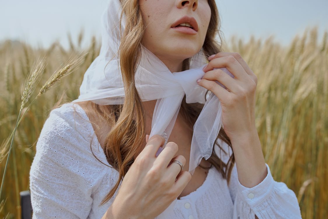 Free Crop woman in white headscarf sitting on grassy field Stock Photo
