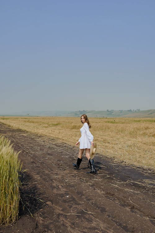 Stylish woman walking on rural road in field