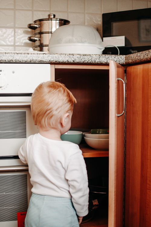 Free Curious toddler exploring kitchen cabinet, reaching for bowls. Captures innocence and exploration. Stock Photo