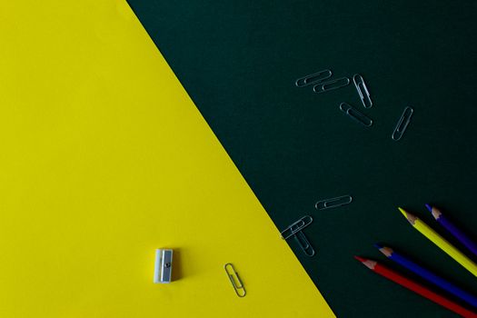 A still life of colored pencils and paper clips on a yellow and green background, perfect for educational themes.