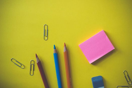 A top view of colored pencils and stationery on a vibrant yellow surface.