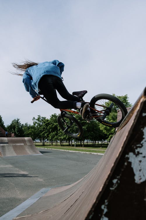 A Person in Denim Jacket Riding Bicycle while Doing Tricks on a Ramp