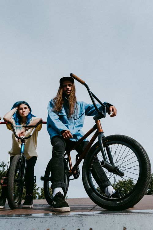 Free Young adults with long hair and vibrant fashion pose confidently with BMX bikes under a clear sky. Stock Photo