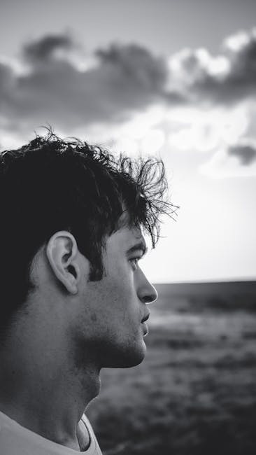 Monochrome side profile portrait of a man outdoors with dramatic sky.